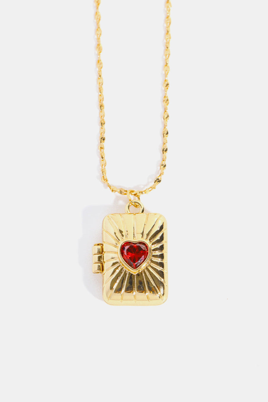 Gold locket pendant necklace with sunburst detail and red heart gem