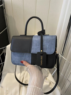 Chic two-tone black and blue PU leather crossbody handbag with top handle and tag.