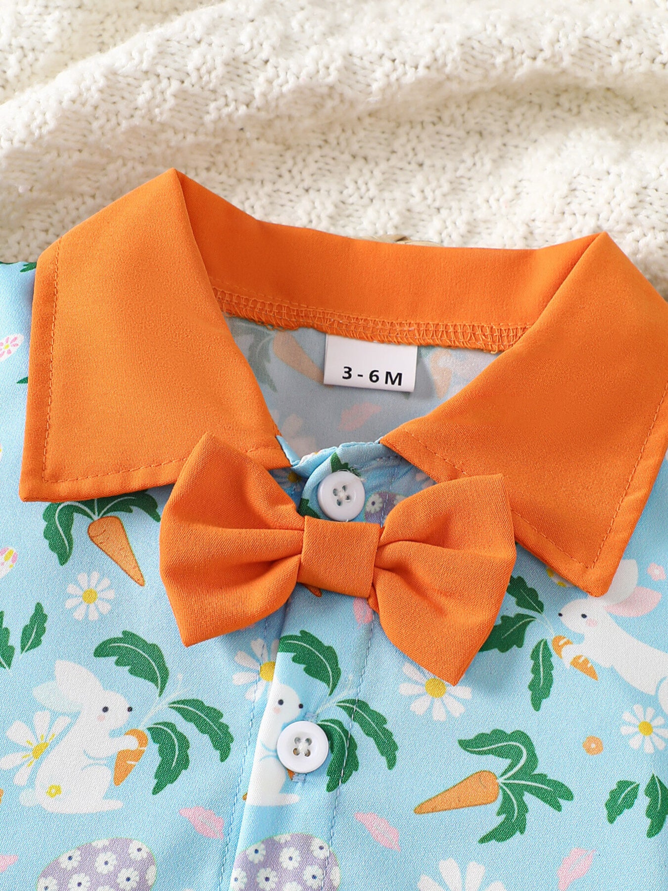 Baby bodysuit with orange collar and bow, featuring a blue bunny and carrot print.