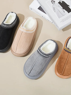 Embroidered trim shearling house slippers in gray, caramel, tan, and black with plush lining.
