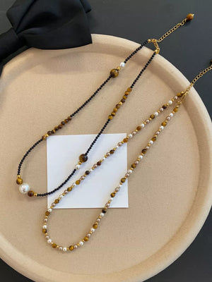 Layered necklaces with tiger eye beads, pearls, and gold accents on black and camel chains.