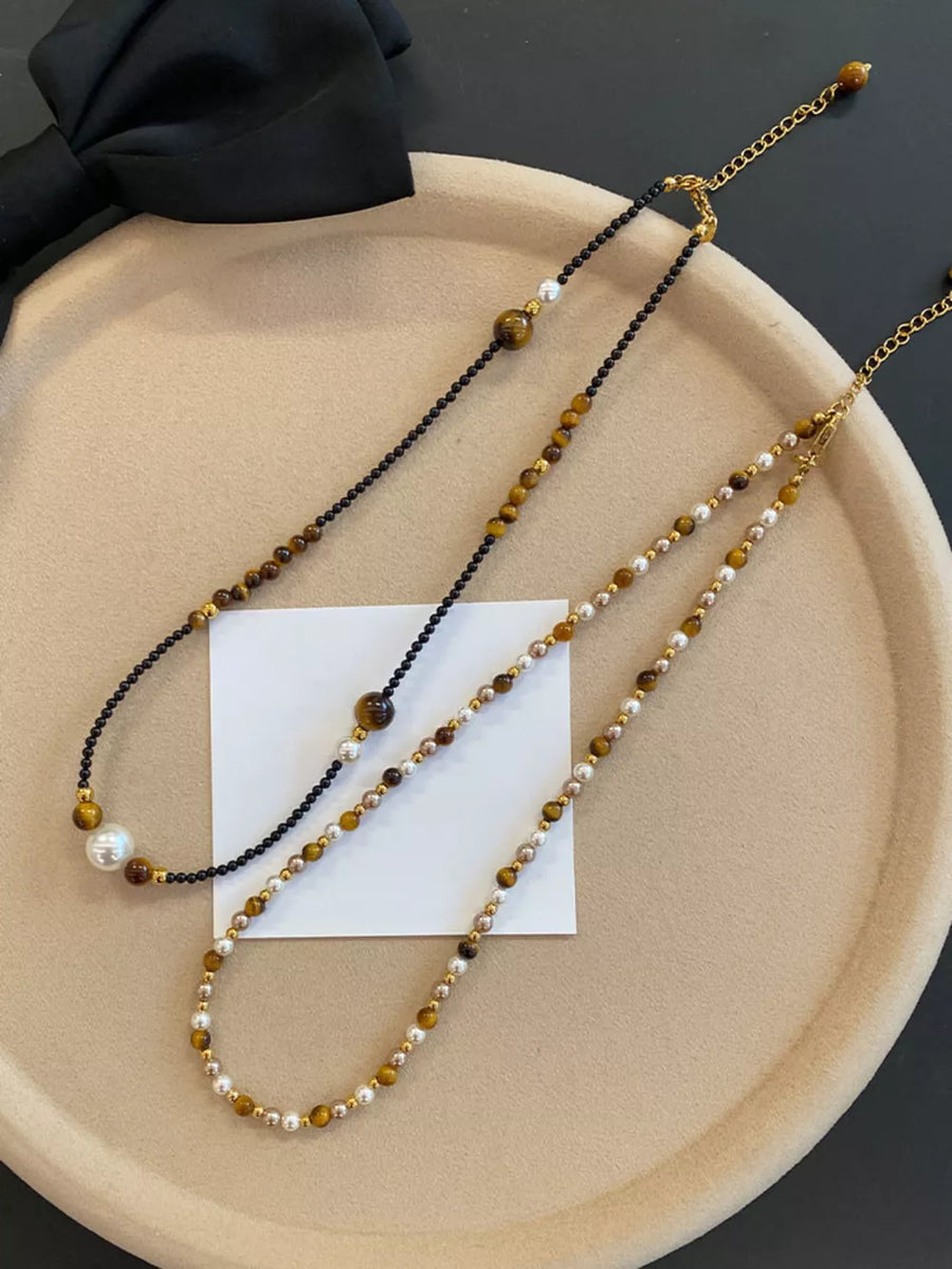 Layered necklaces with tiger eye beads, pearls, and gold accents on black and camel chains.