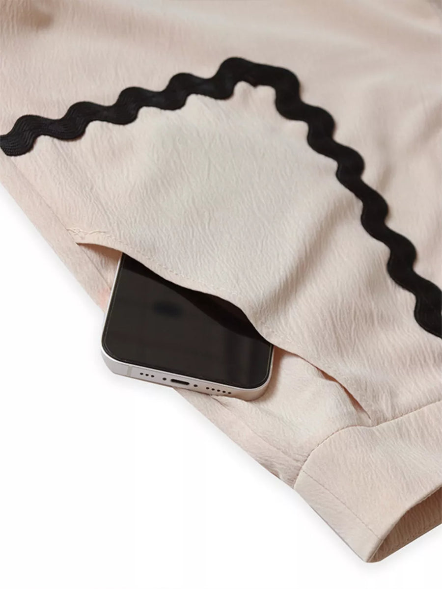 Scalloped trim pajama shorts in light pink with black wavy trim and a pocket holding a phone.