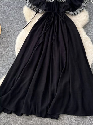 Black embroidered V-neck maxi dress with a tie waist and flowing skirt.