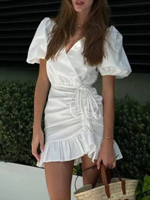 White wrap dress with puff sleeves, ruched detail, drawstring, and ruffled hem