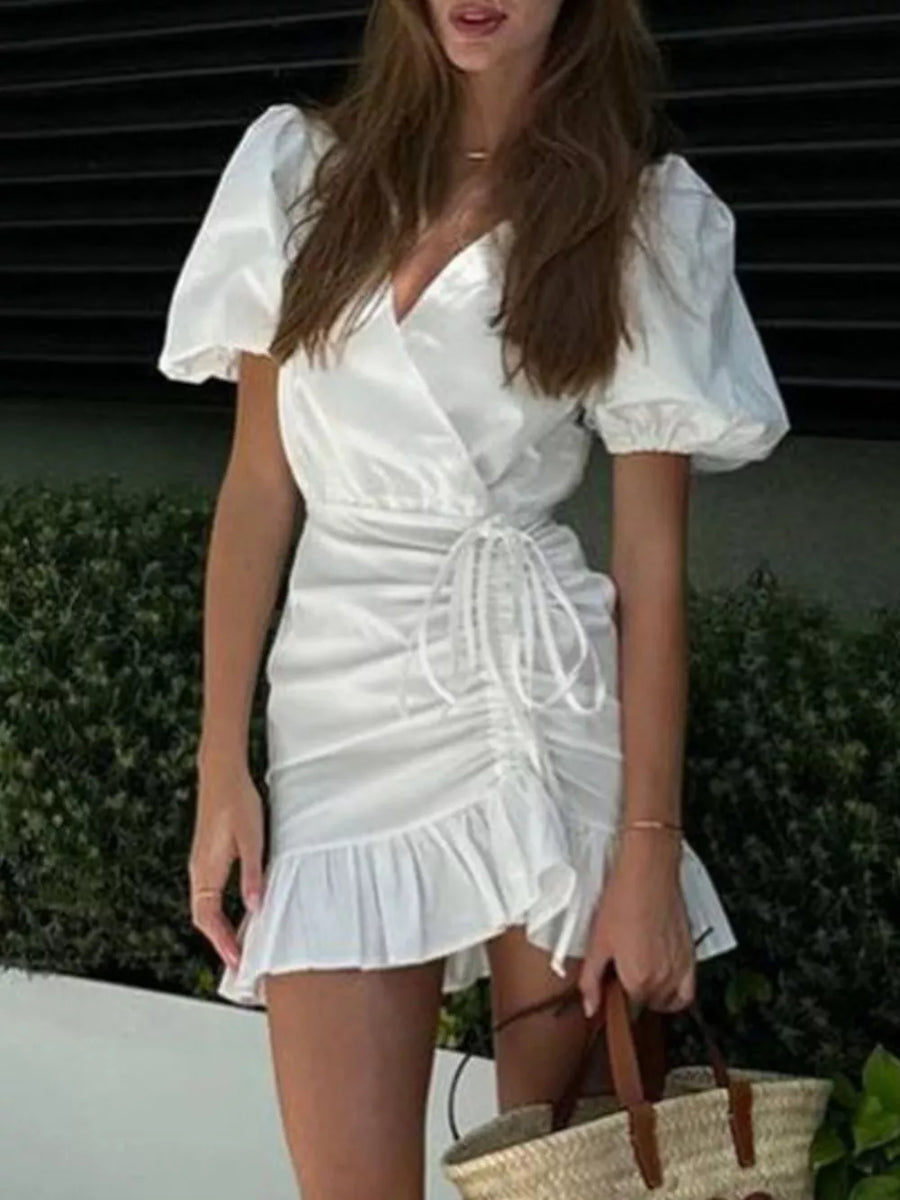 White wrap dress with puff sleeves, ruched detail, drawstring, and ruffled hem