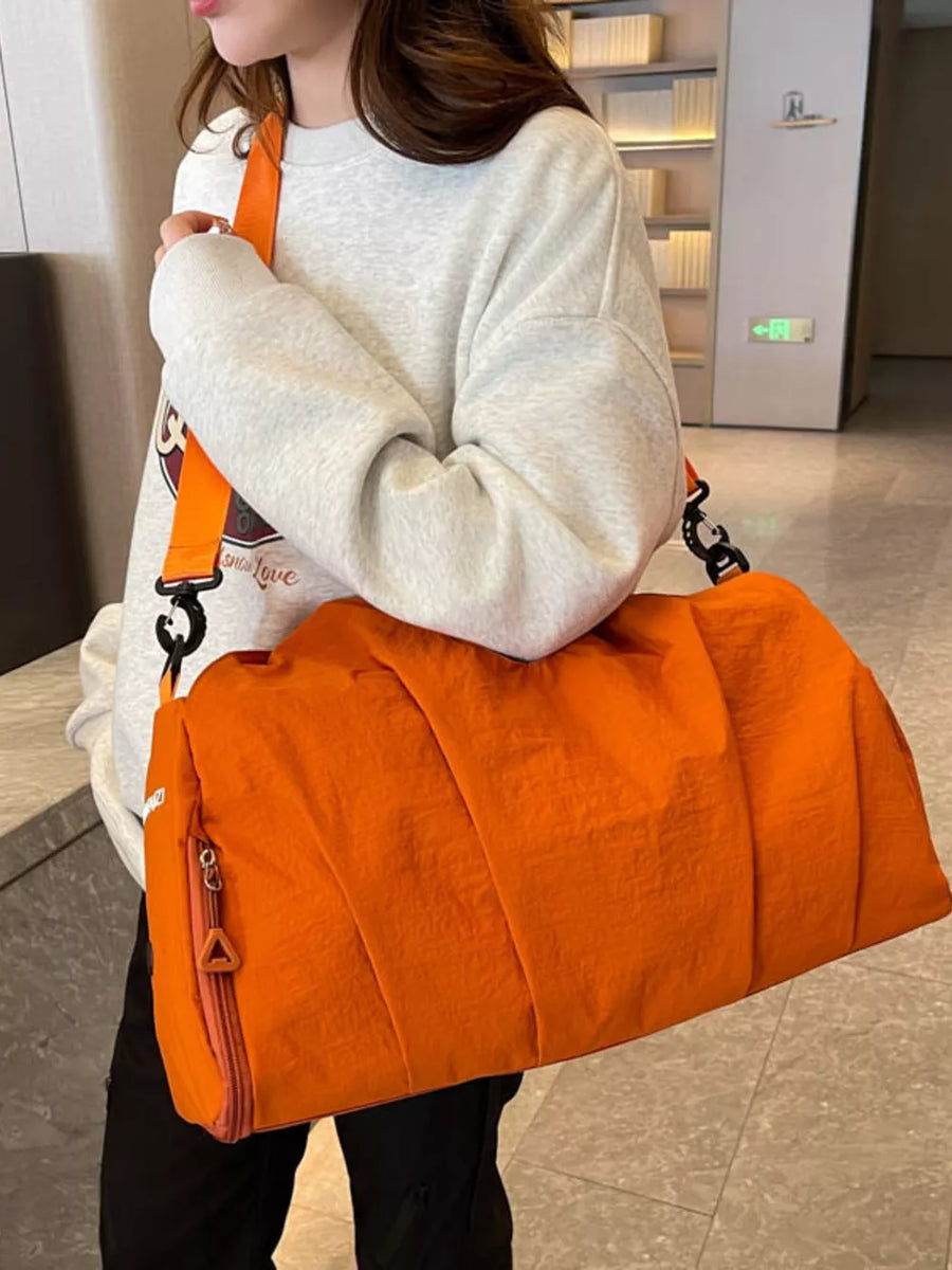 Orange nylon duffel bag with pleated detail and zip pocket, worn with a grey sweatshirt.