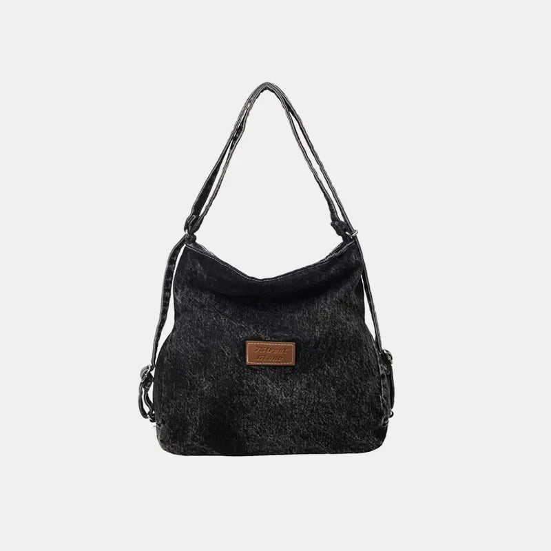 Black denim hobo bag with leatherette patch and adjustable straps.