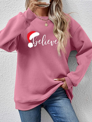 Blush pink raglan sweatshirt with white "Believe" graphic and Santa hat detail.