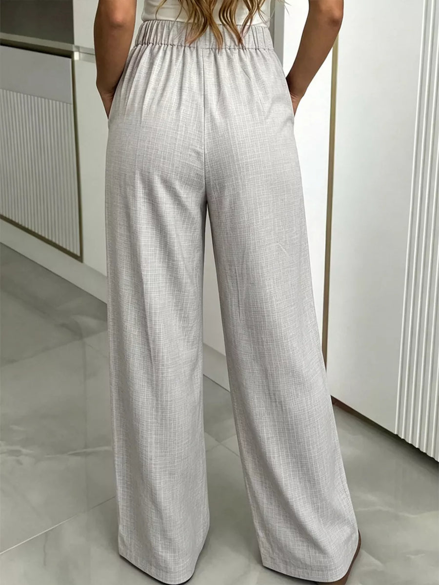 Gray high-waisted wide-leg pleated trousers with a textured fabric and elastic waistband.
