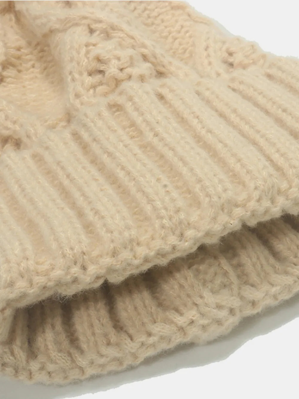 Beige cable knit acrylic beanie with ribbed cuff detail.