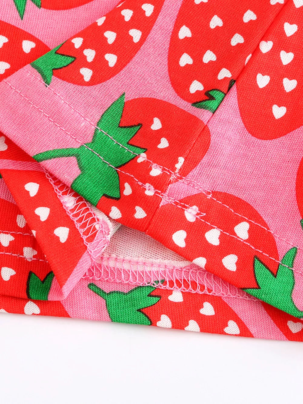 Baby dress with allover red strawberry print on pink cotton blend fabric.