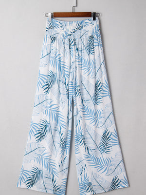 Tropical leaf print wide leg pants in white with blue foliage pattern and smocked waist.