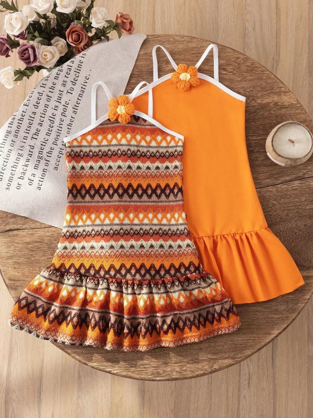 Baby halter dresses with ruffled hems, one orange, one patterned with orange, brown, and white.