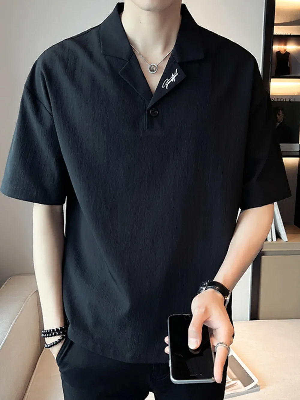 Black cotton polo with embroidered detail on collar, buttoned placket, and short sleeves.