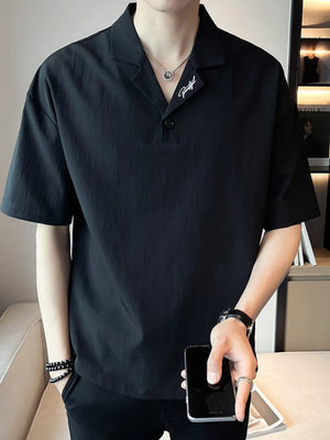 Black cotton polo with embroidered detail on collar, buttoned placket, and short sleeves.