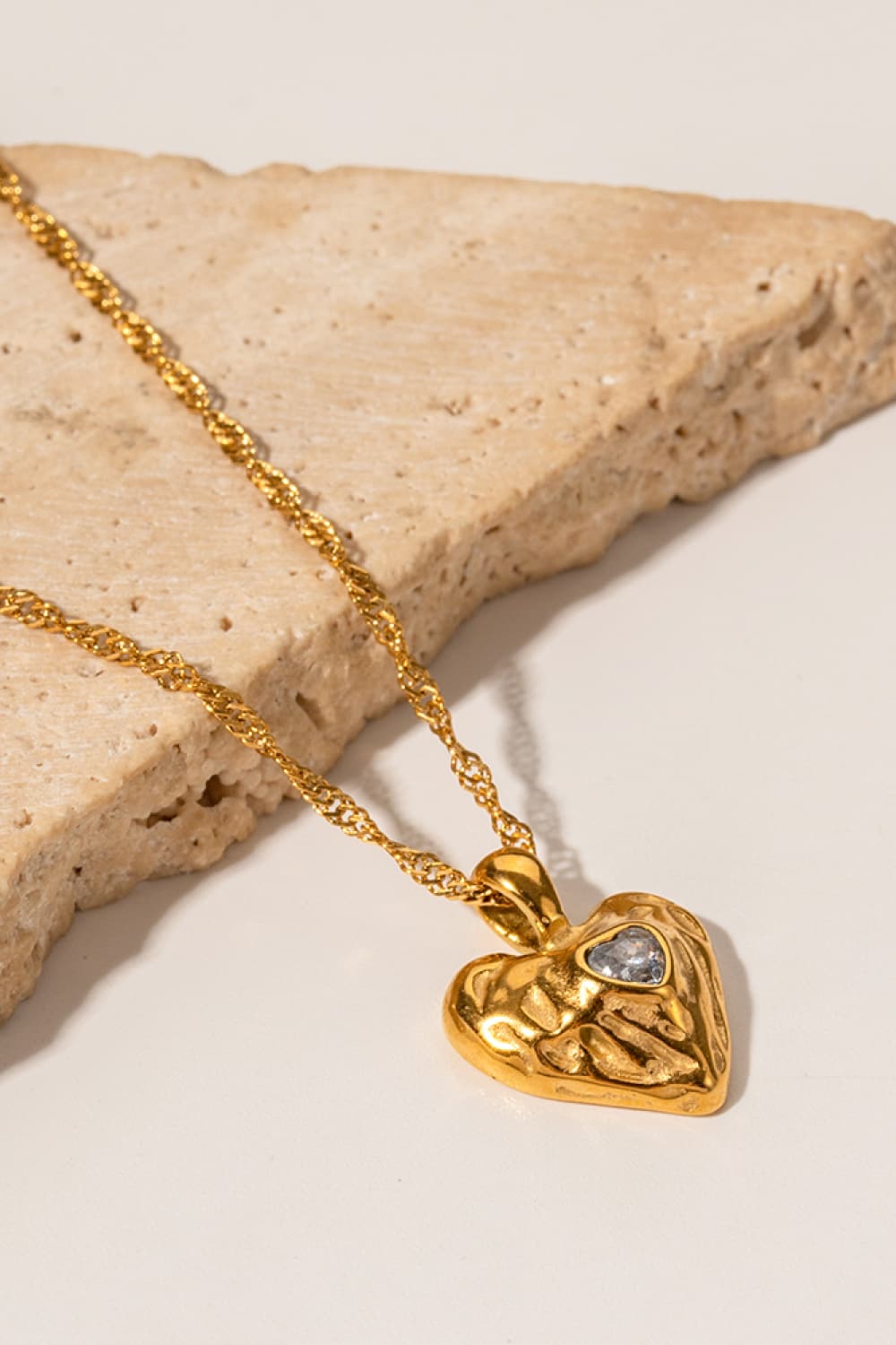 Gold textured heart pendant necklace with a small blue stone on a twisted chain.