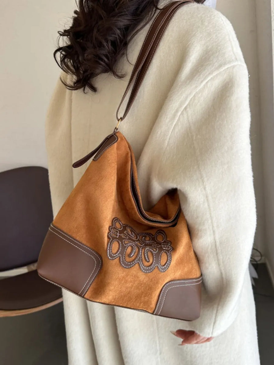 Ochre suede hobo bag with brown leather trim, appliqué detail, and contrast stitching.