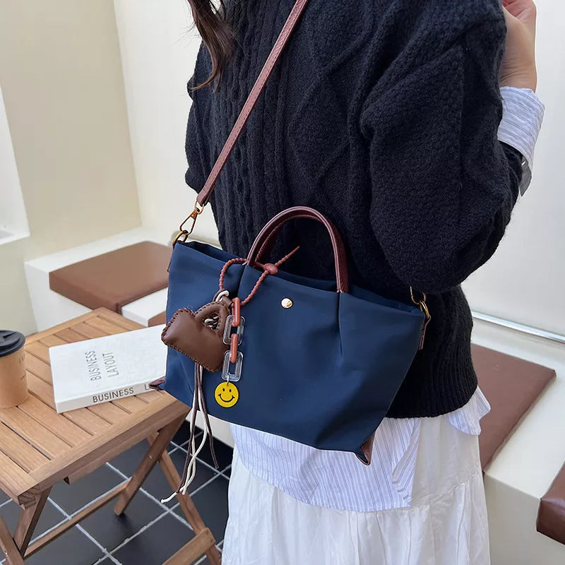 Compact dark blue nylon handbag with leather handles and charm details.
