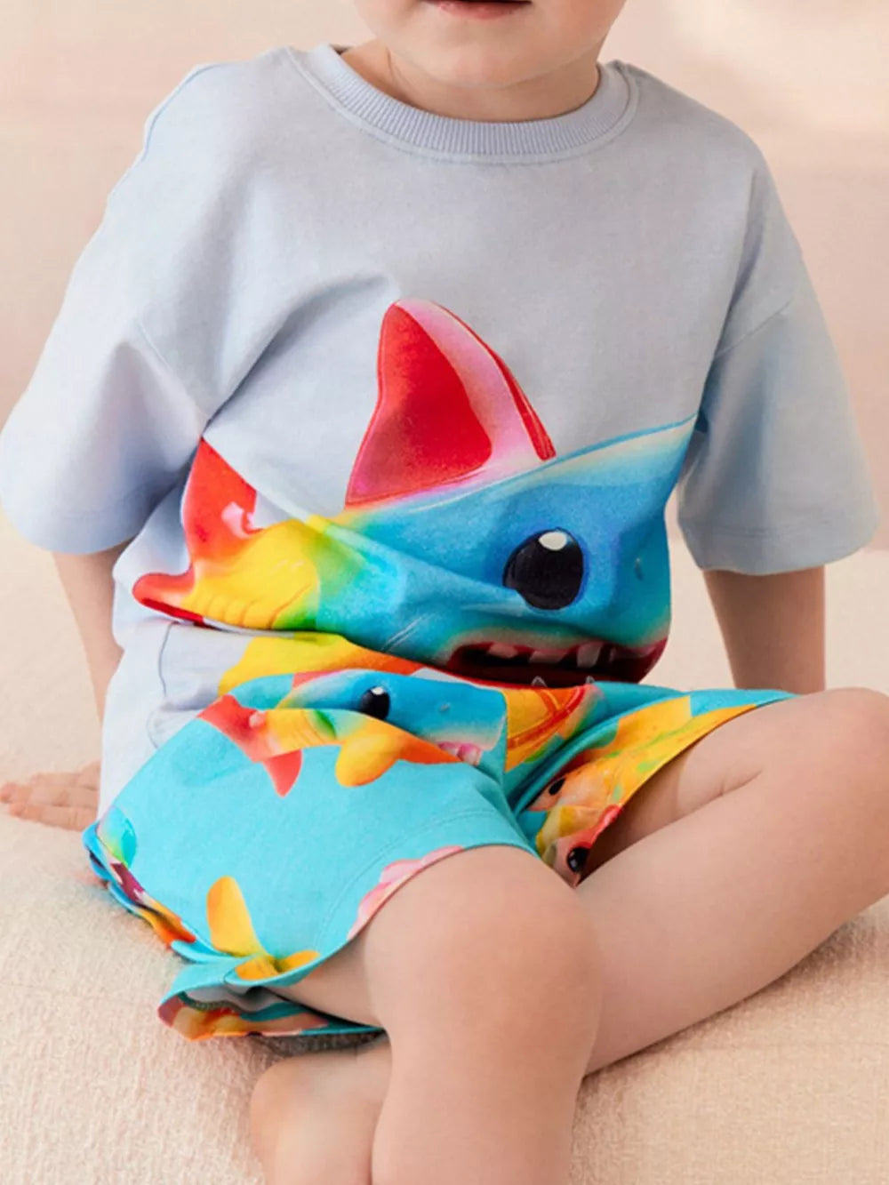 Light blue cotton blend toddler boys' set with vibrant rainbow shark print shorts and matching tee.