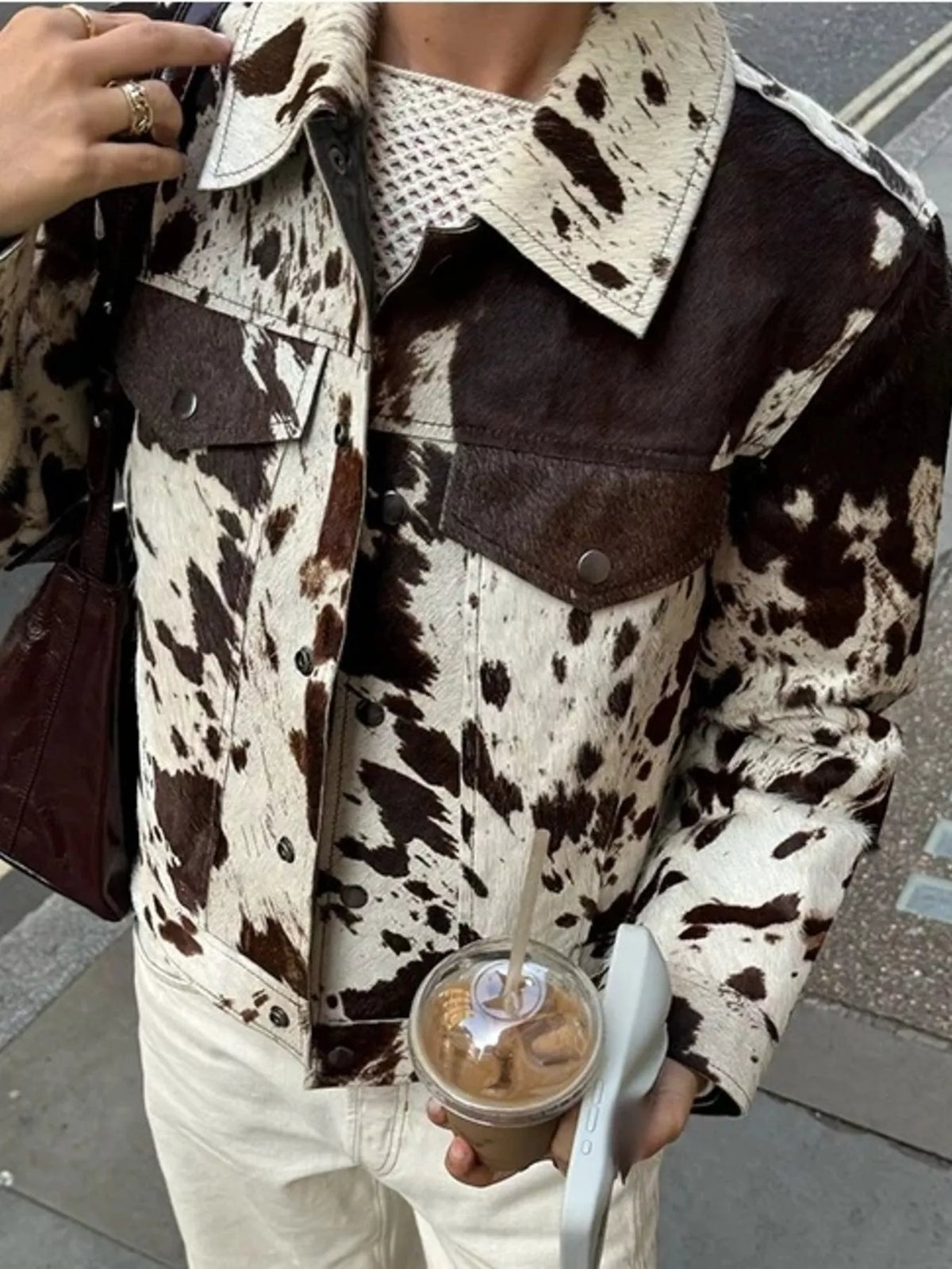 Buttoned collared cow print jacket with chest pockets and button front closure.