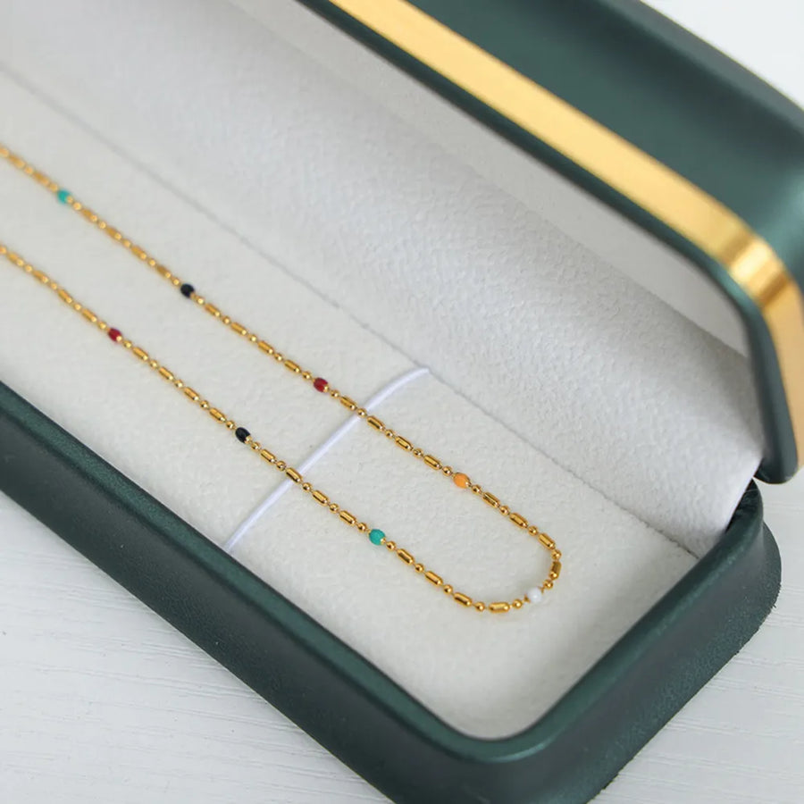 Gold chain necklace with colorful enamel beads and bar details in a jewelry box