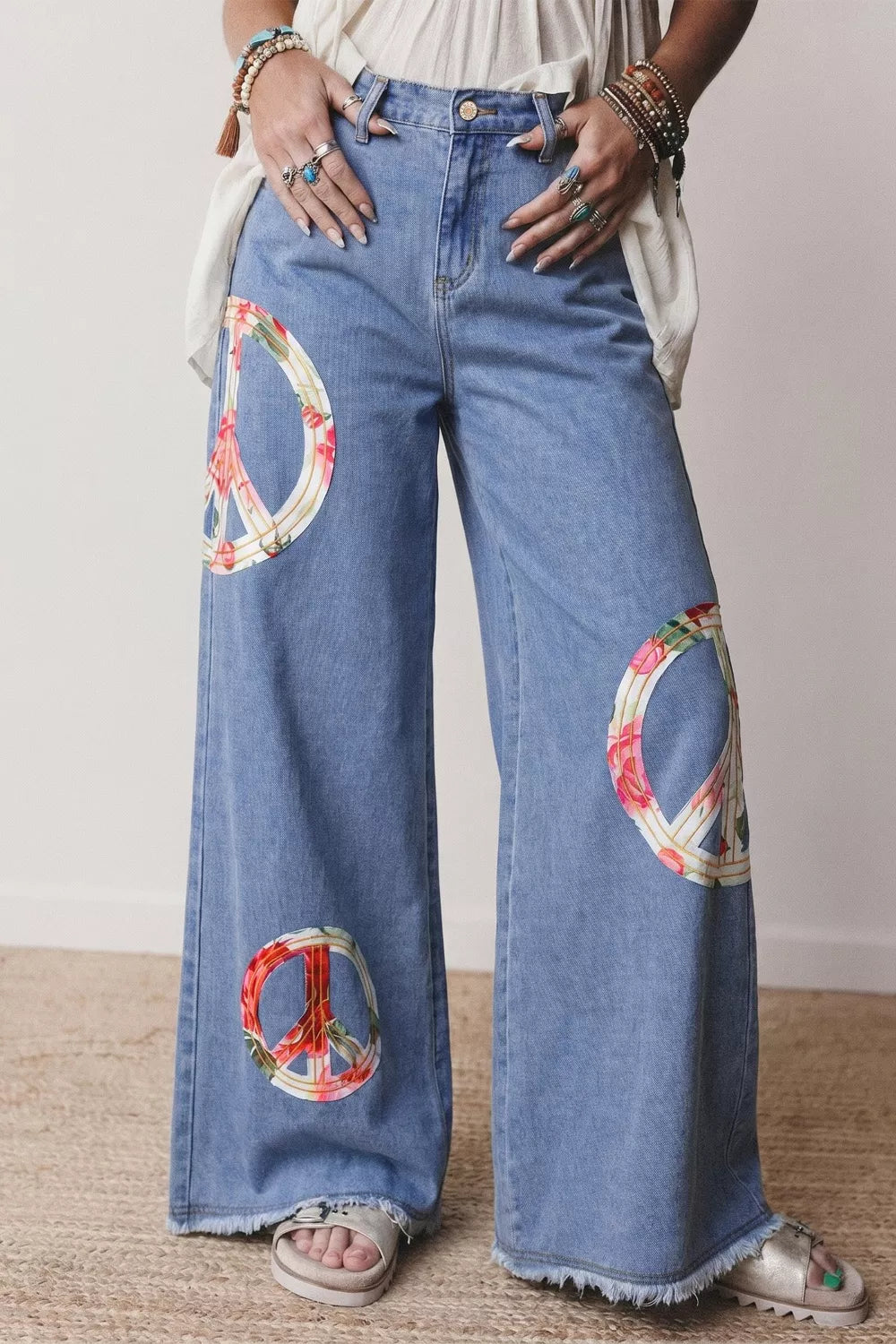 Light wash denim wide-leg jeans with floral peace sign appliqués and frayed hem.