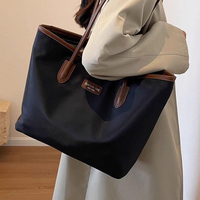 Large black Oxford cloth tote bag with brown trim and handles.