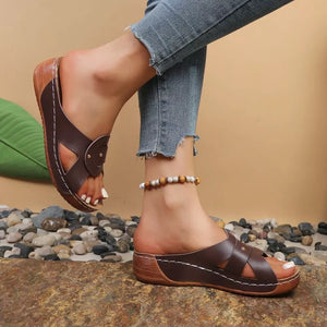 Brown slip-on wedge sandals with crisscross straps and riveted detail.