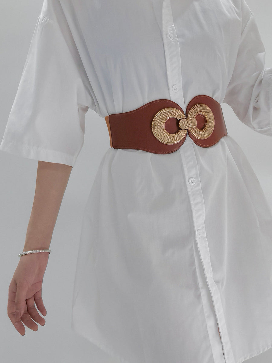 Caramel elastic belt with gold interlocking circle buckle cinching a white shirt