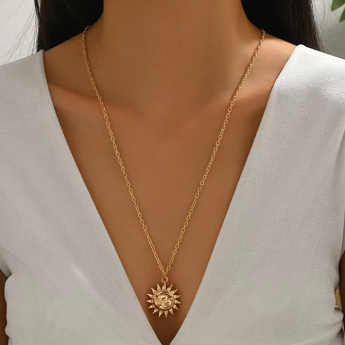 Gold sunburst pendant necklace with a detailed face, on a delicate chain.