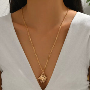 Gold sunburst pendant necklace with a detailed face, on a delicate chain.