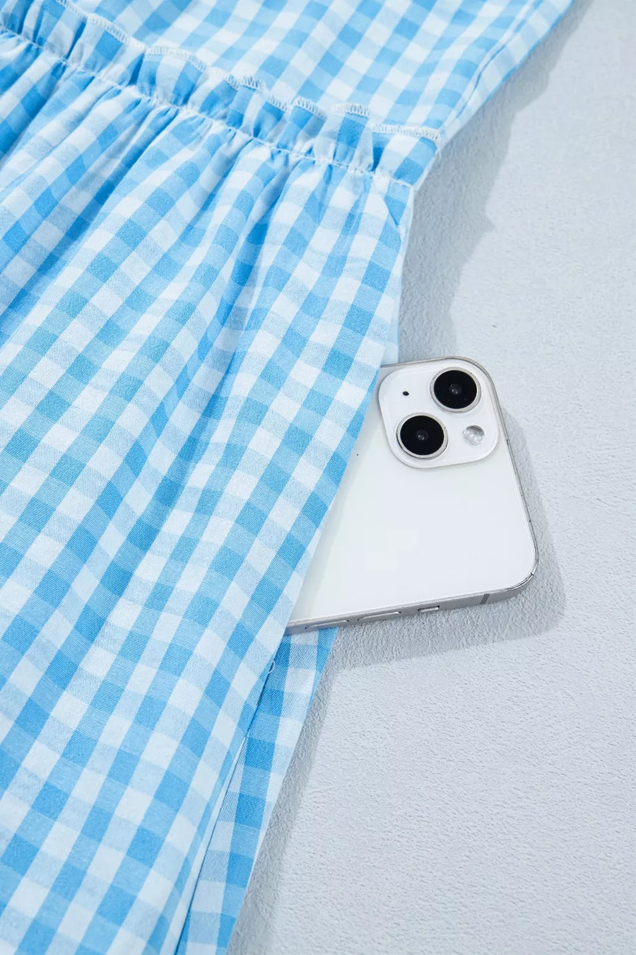 Blue gingham tiered maxi dress with ruffled waist and side pocket holding a phone.