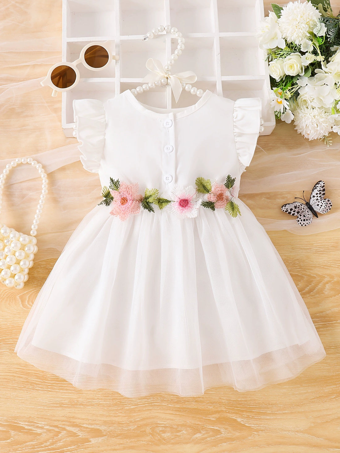 White baby dress with floral appliqué belt, ruffle sleeves, and button front.
