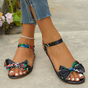 Floral bowknot flat sandals in black with colorful print and ankle strap.