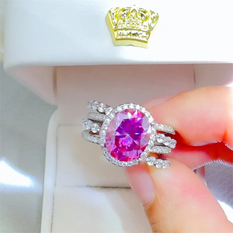 Silver ring with oval pink gem surrounded by halo of small diamonds and stacked band details.