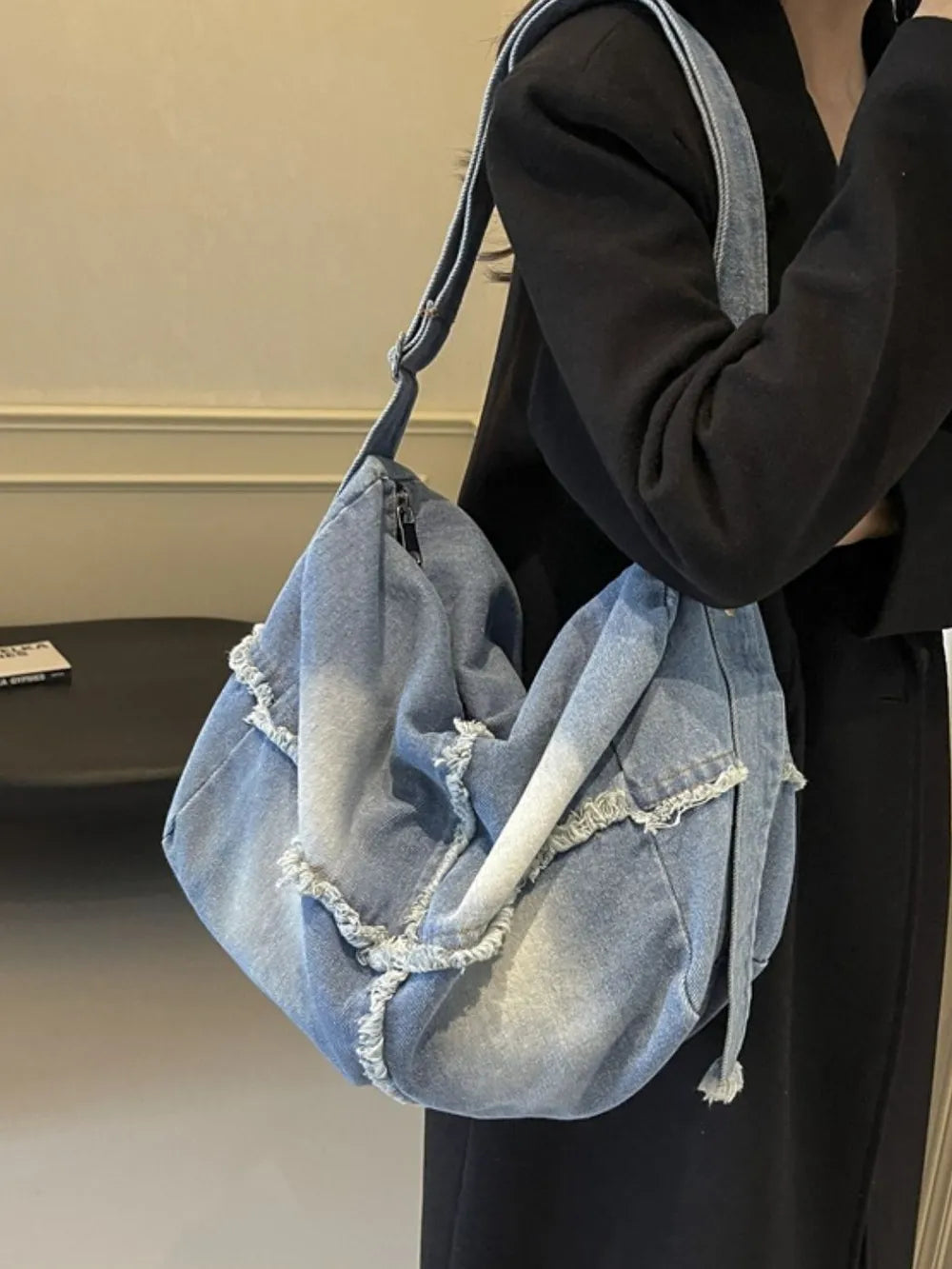 Frayed denim slouch crossbody bag in light wash with distressed edges and a casual silhouette.