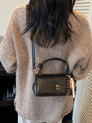 Black leather crossbody bag with beaded charm and top handle.