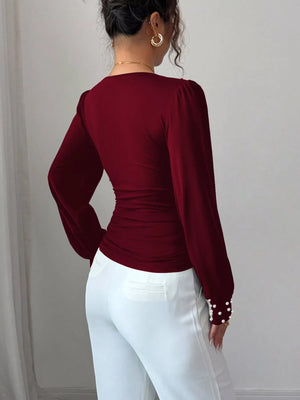Burgundy ruched V-neck blouse with pearl embellished cuffs and puff sleeves.