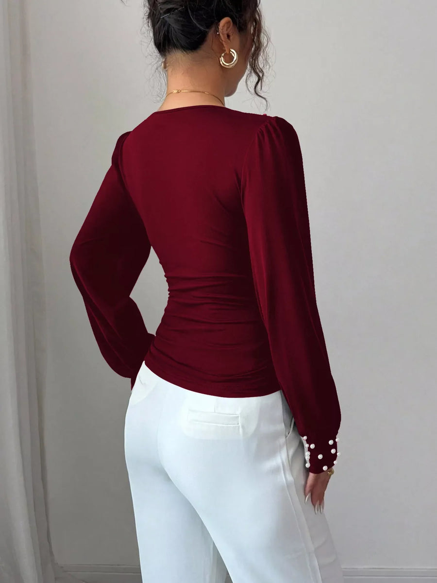 Burgundy ruched V-neck blouse with pearl embellished cuffs and puff sleeves.
