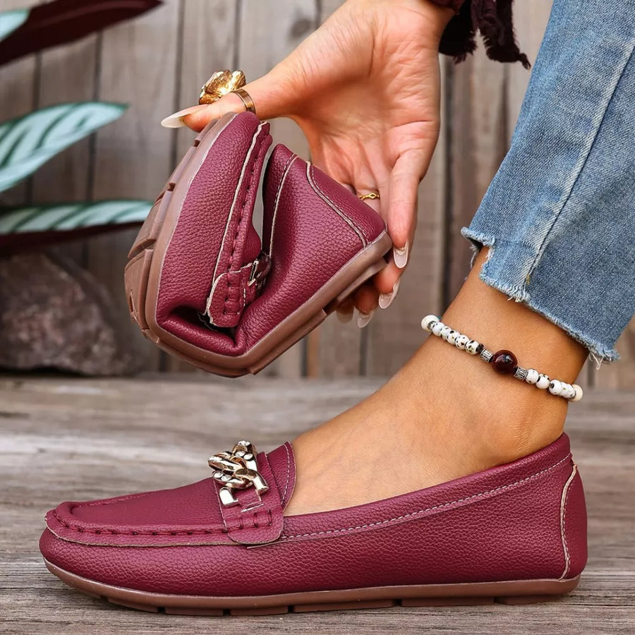 Burgundy round-toe loafers with gold chain detail and flexible sole.