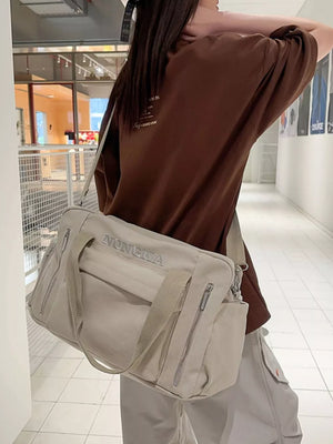 Beige canvas duffel bag with adjustable crossbody strap and zippered pockets.