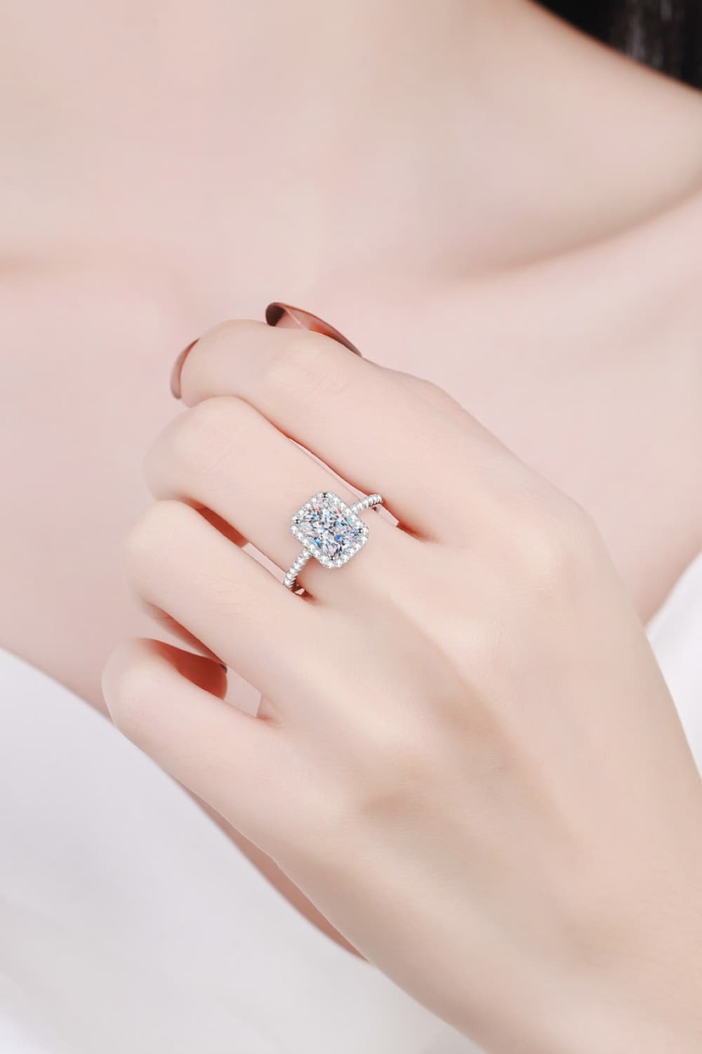 Radiant cushion cut halo ring in silver with sparkling stones on a hand.