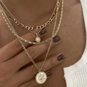 Layered gold coin pendant necklace with sunburst charm and diamond accent.