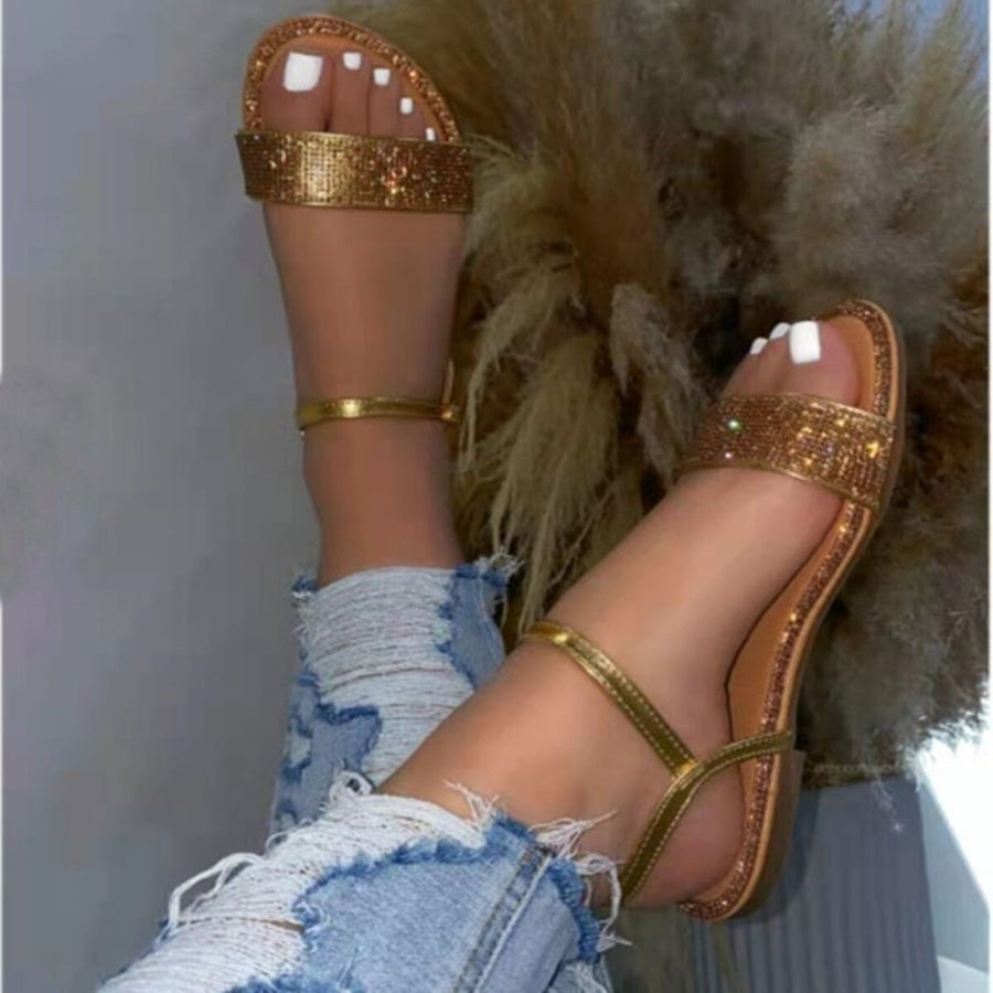 Gold rhinestone-embellished flat ankle sandals with delicate straps and distressed jeans.