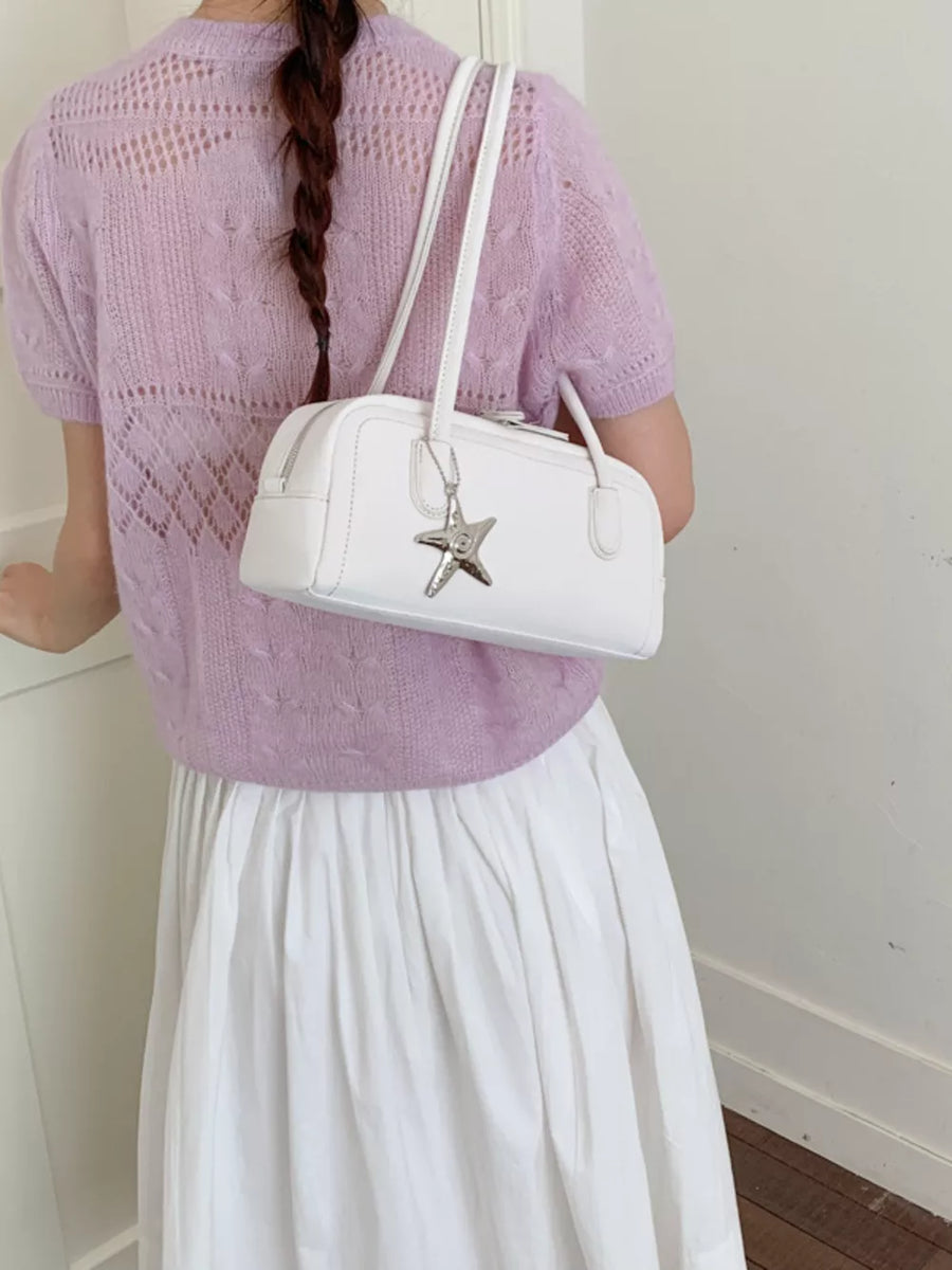 White shoulder bag with star charm detail, worn by a woman in a lilac knit top.