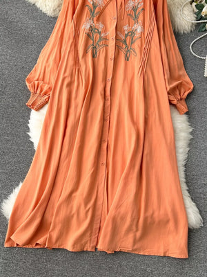 Orange cotton maxi dress with embroidered floral detail and tie neck.