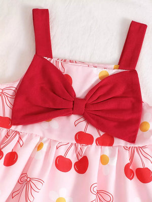 Baby dress in pink with cherry print, featuring red straps and a large red bow detail.