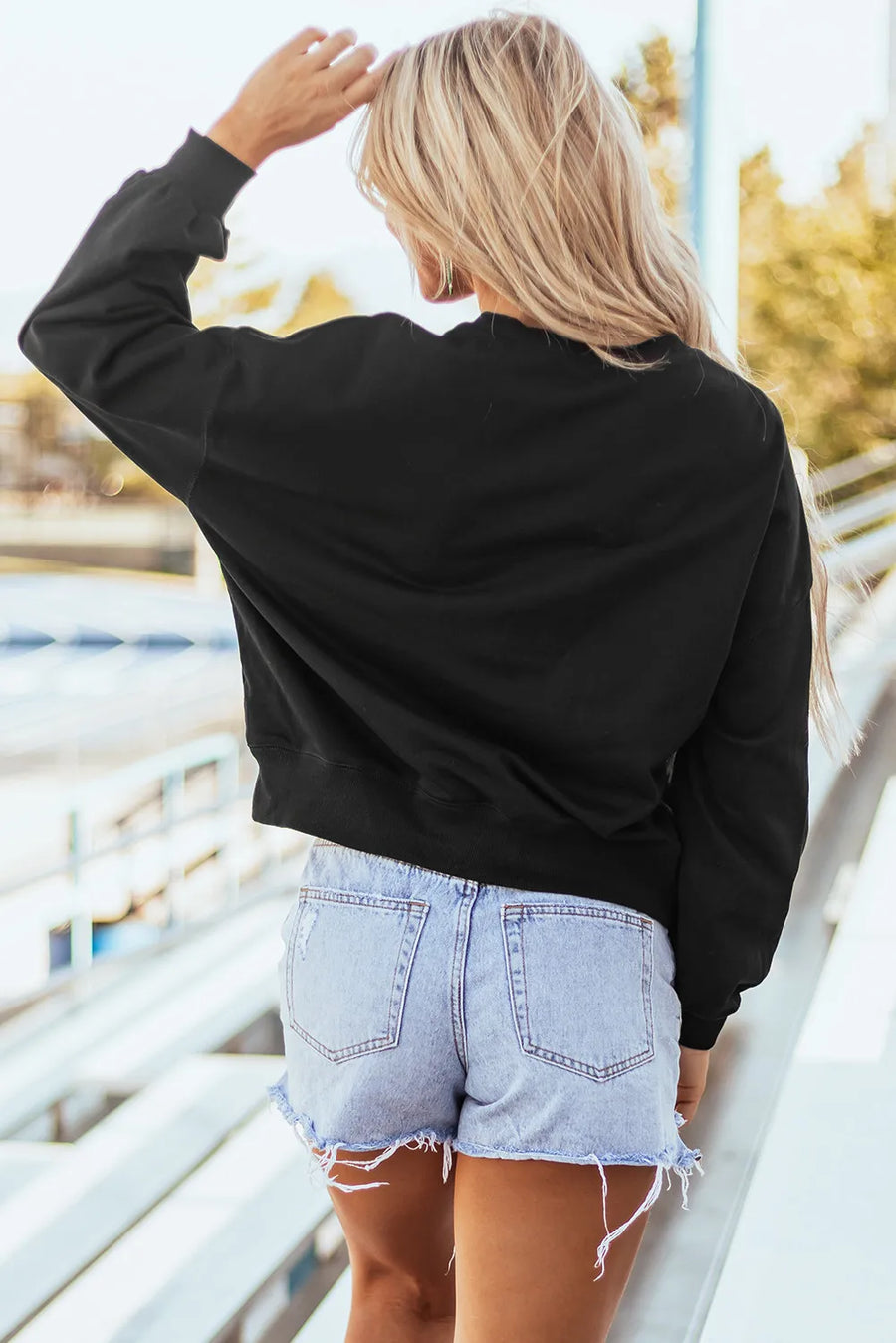 Black crewneck sweatshirt with long sleeves and a relaxed fit, worn with denim shorts.
