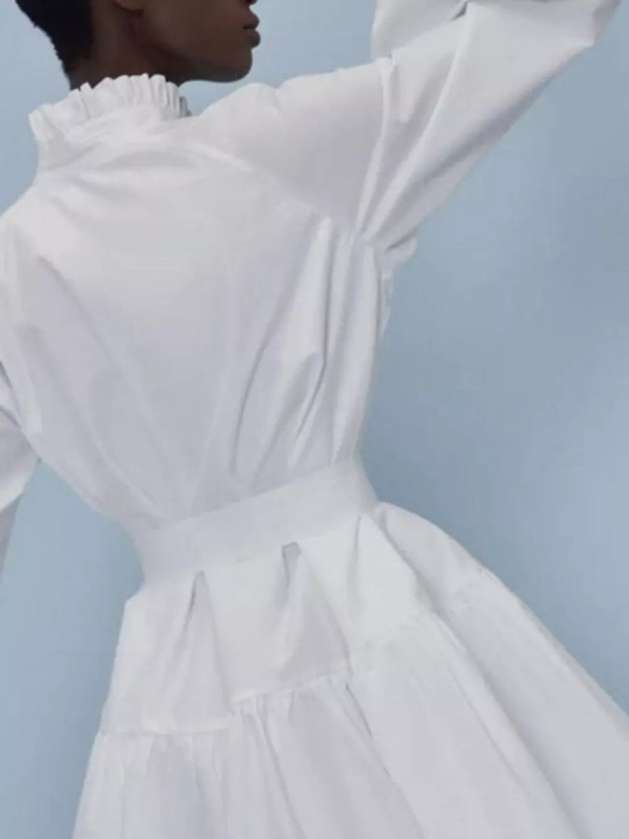 White cotton dress with ruffled high neck, long sleeves, belted waist, and tiered skirt.